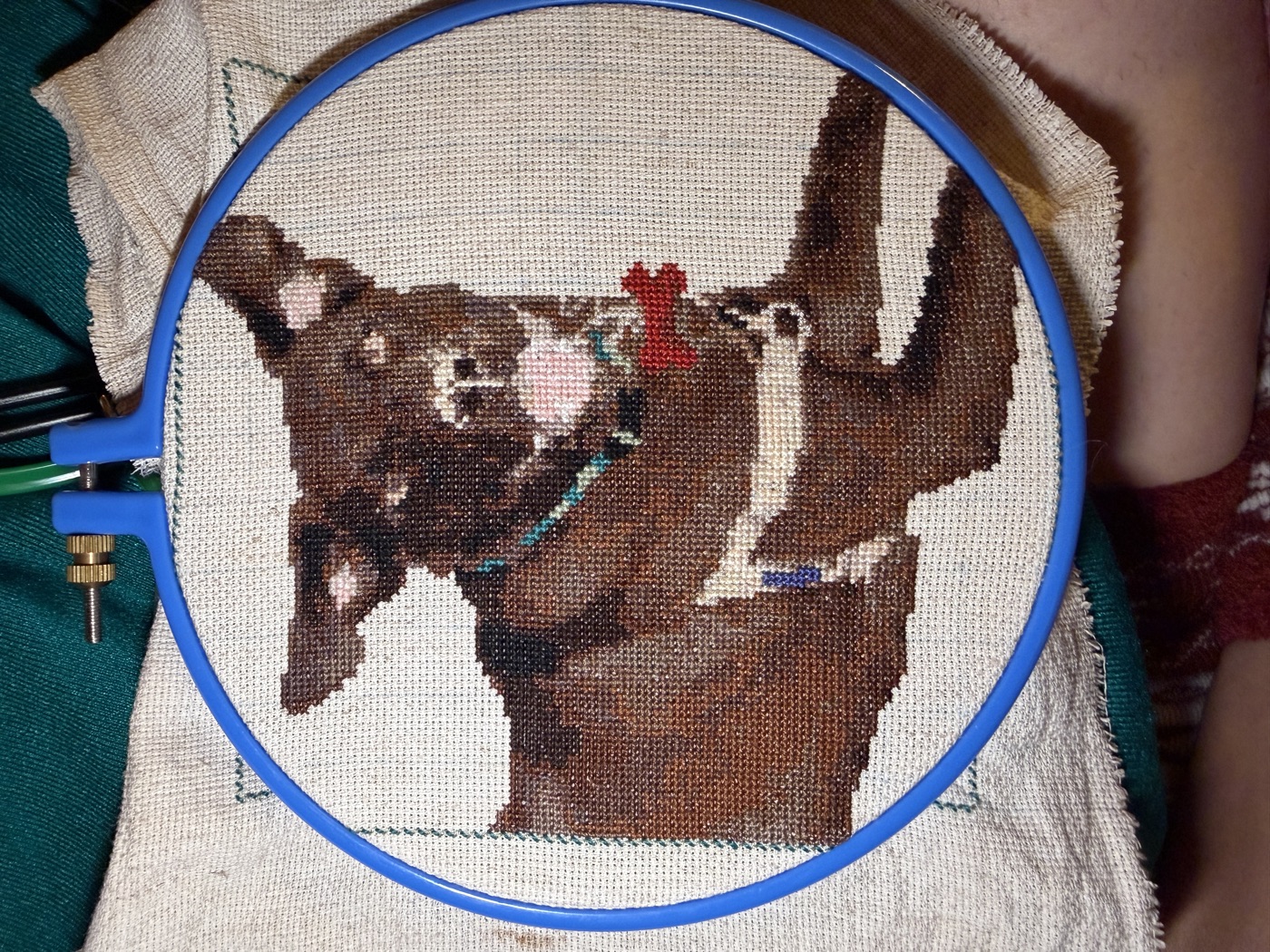 Cross-stitch embroidery in a blue hoop showing a portrait of two people in brown and cream tones.