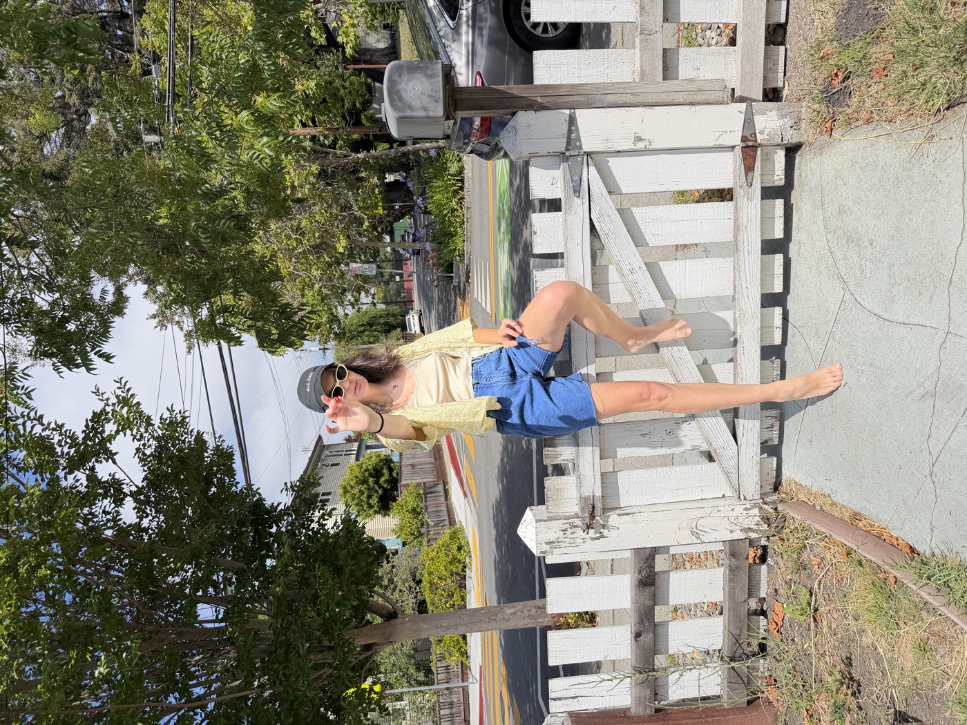 A person with arms outstretched stands near a rainbow-striped painted structure by a dock.