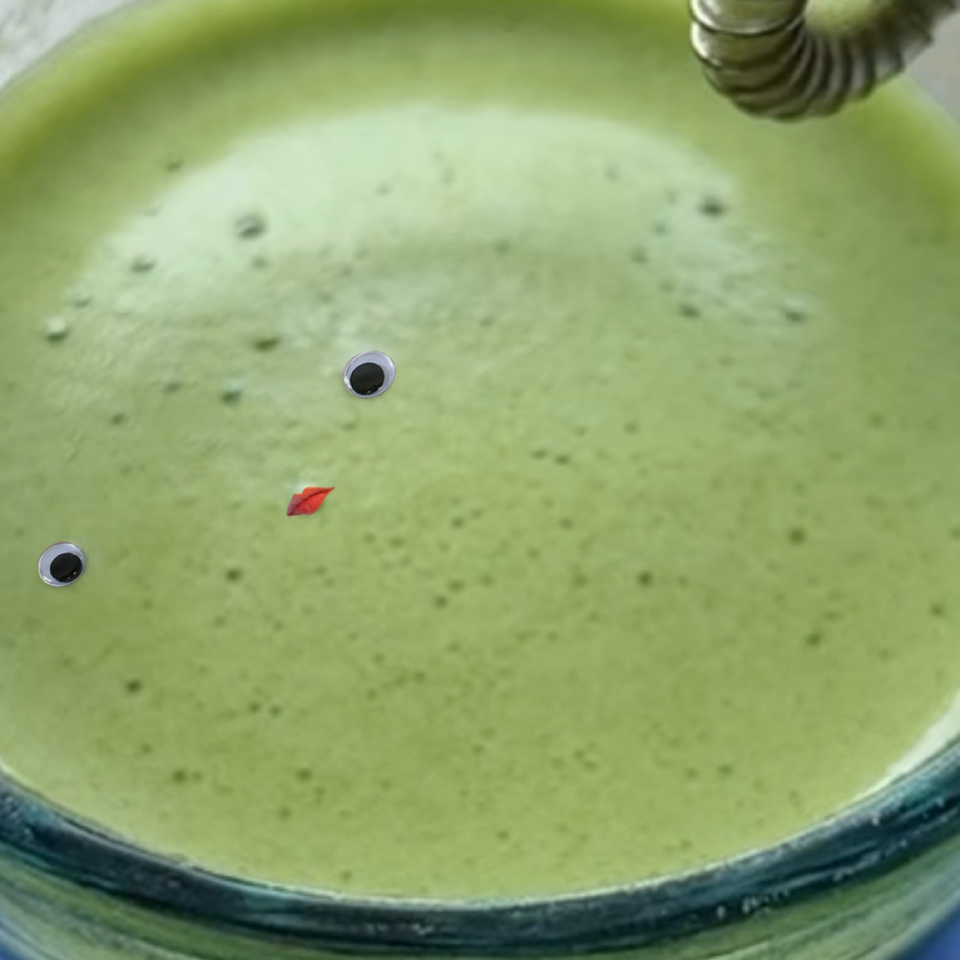 A green matcha drink in a bowl decorated with two googly eyes and a small red leaf.