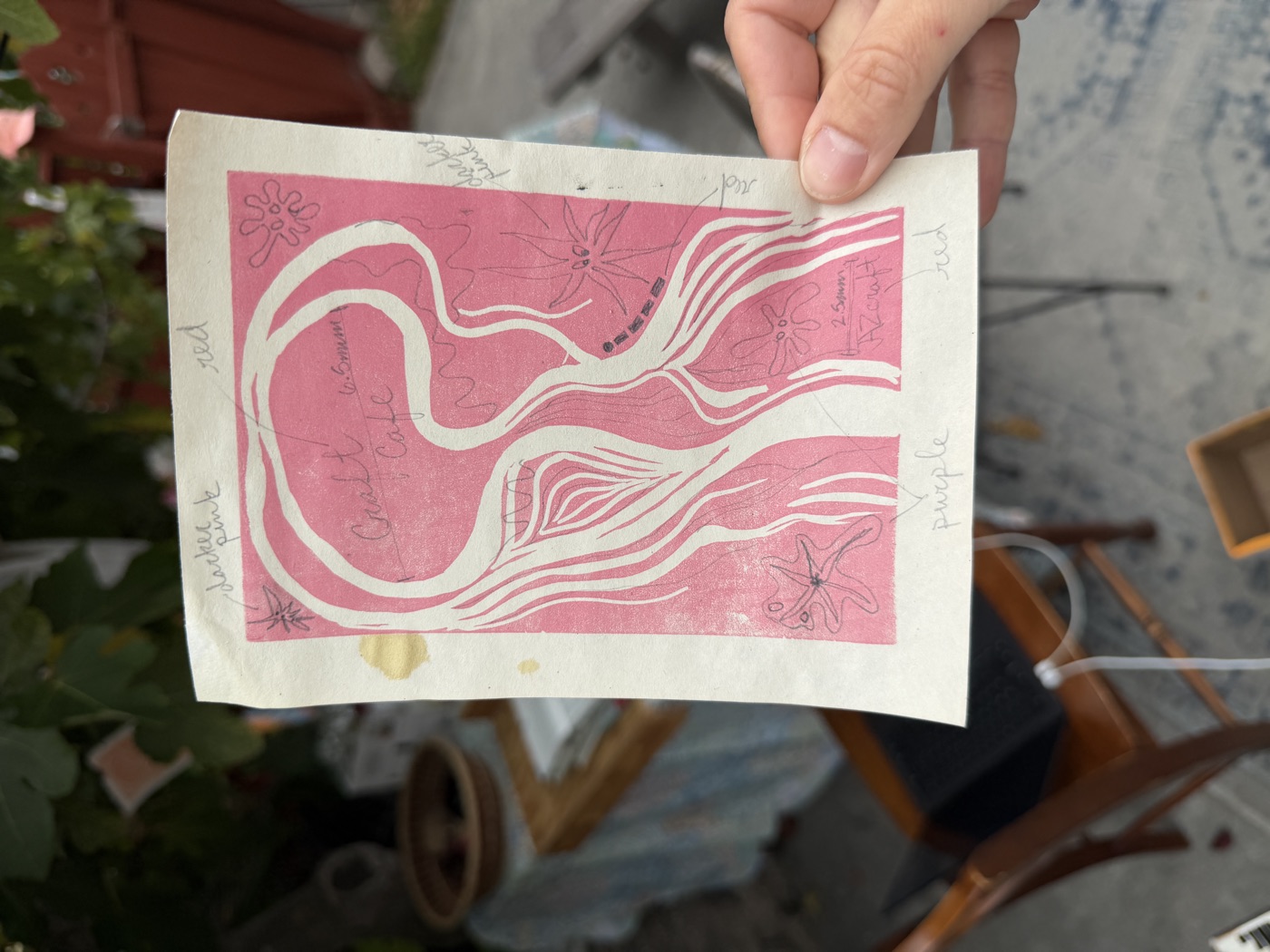 A pink linocut print with white outlines of an abstract flowing figure with floral corner details.