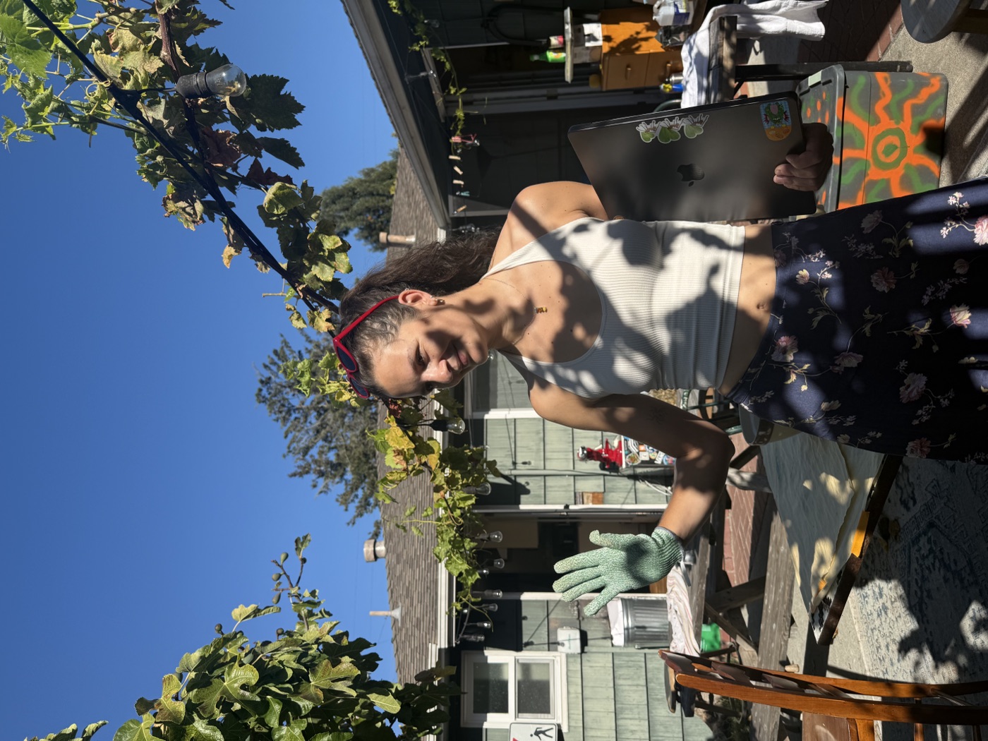 A person in green gloves holds a small craft item while standing in a sunny backyard.