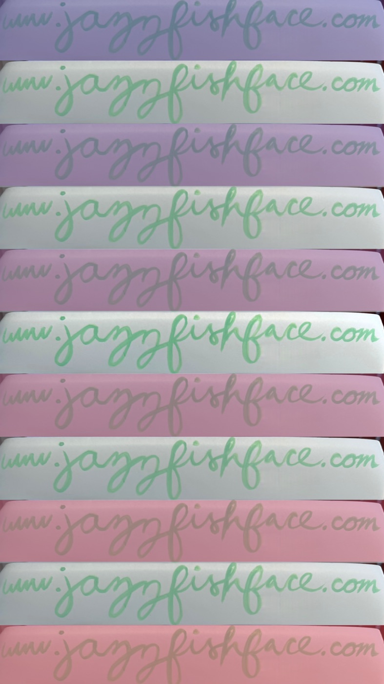 Hand-lettered paper strips in pastel purple, green, and pink, each reading www.jazzyfishface.com in green and purple ink.