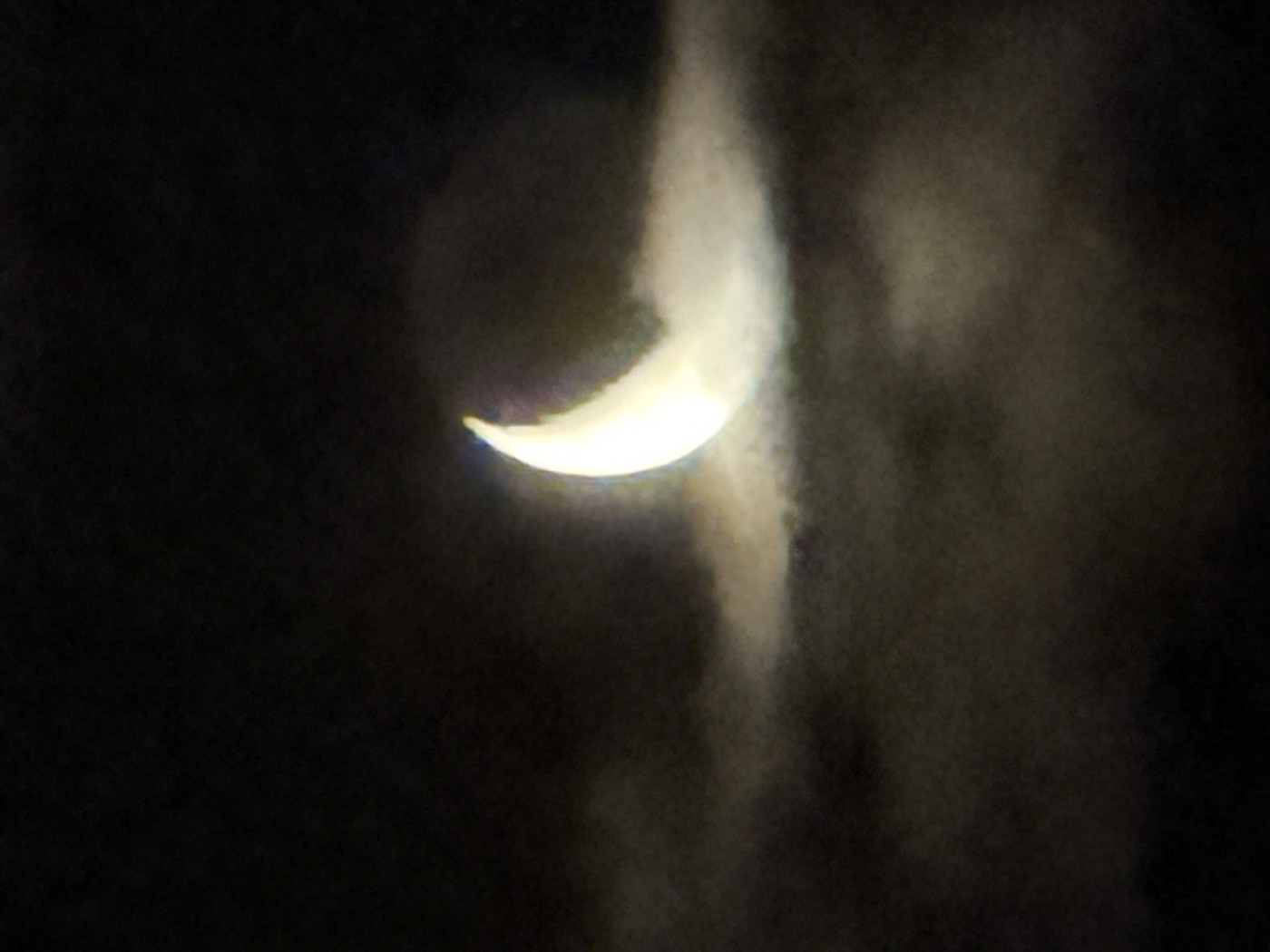 A crescent moon glowing against a dark cloudy sky at night.