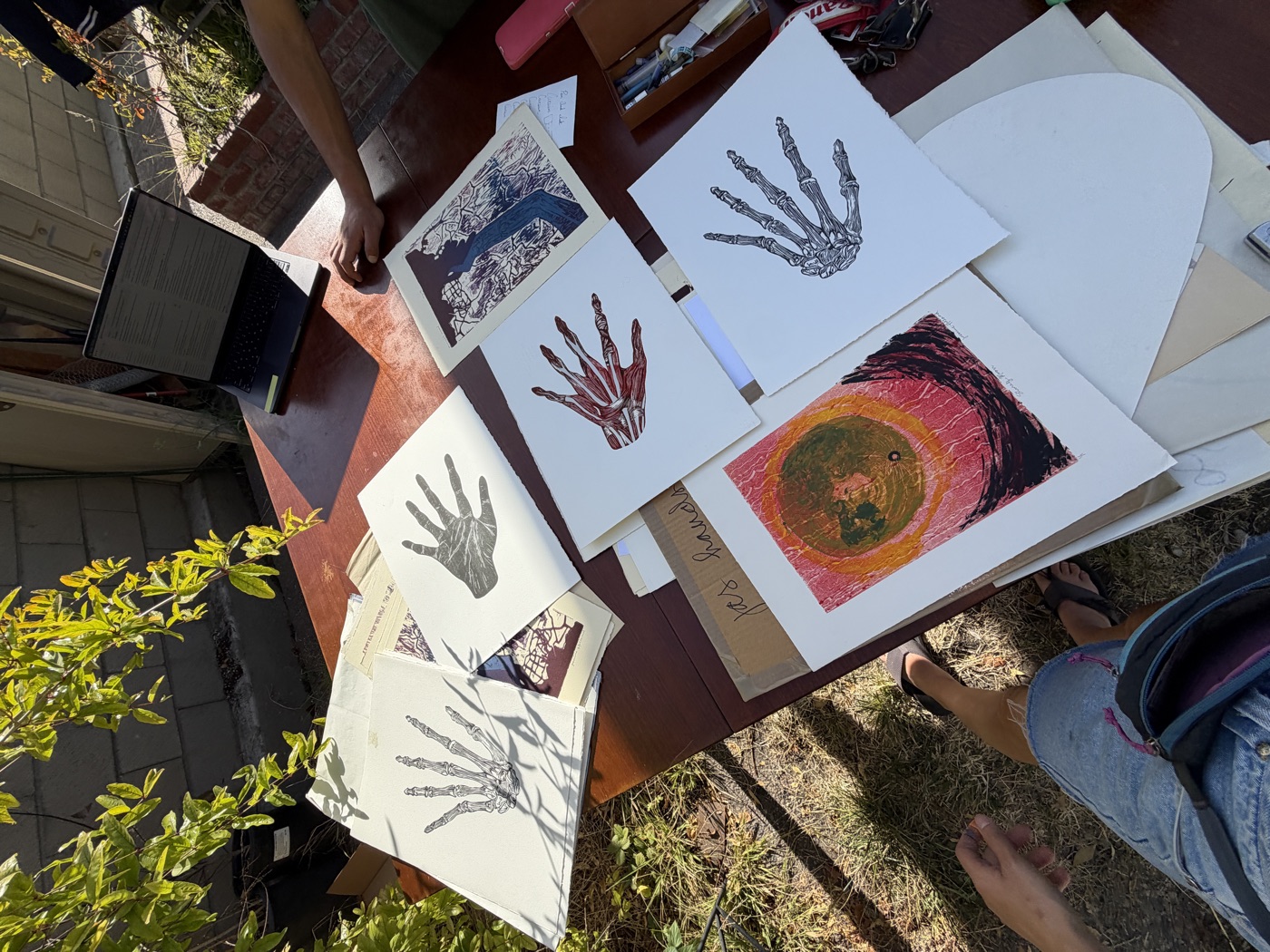 Overhead view of artworks including hand prints and a colourful circular composition, in natural sun.