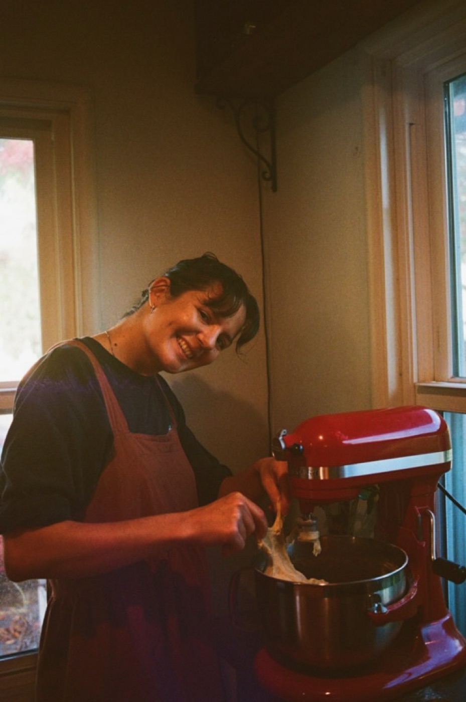A person in an apron using a red stand mixer at a counter.