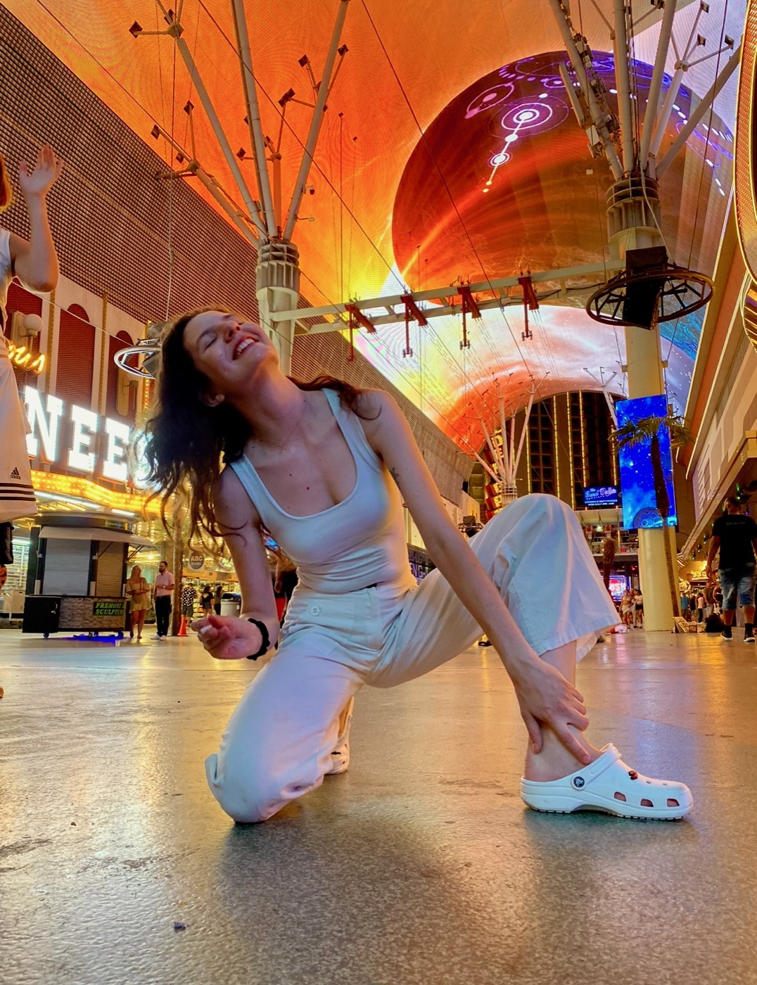 A person in white posing under a colourful neon geometric light installation.