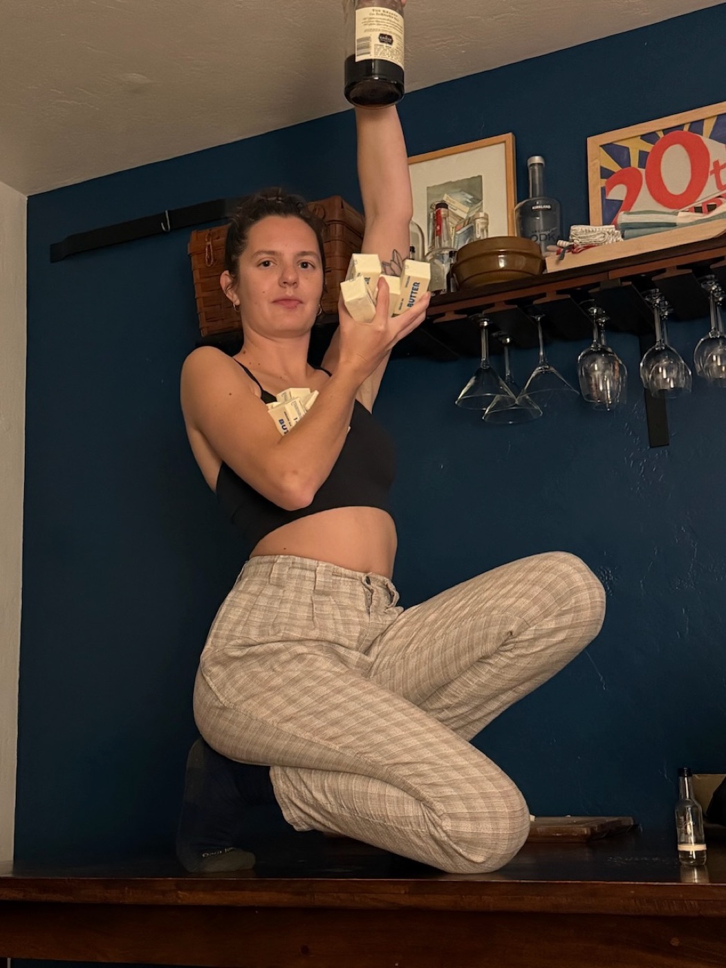 A person sitting on a dark blue counter holding cash, posing playfully indoors.