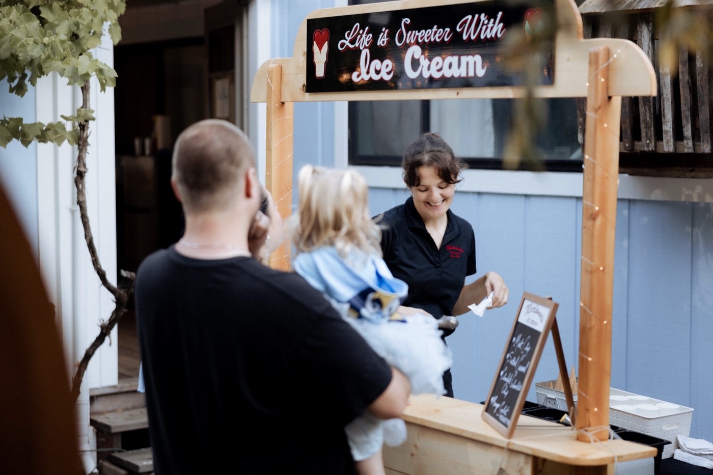 A person serving customers at a wooden ice cream stand with a Life is Sweeter With Ice Cream sign.